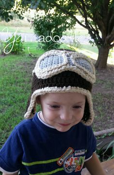 a young boy wearing a crocheted hat on top of a wooden bench in front of a tree