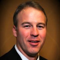 a man in a suit and tie smiling at the camera with a brown background behind him