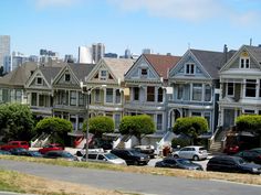 a row of houses with cars parked on the street in front of them and tall buildings