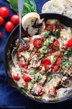 a skillet filled with cheese and tomatoes next to sliced bread on a blue cloth