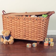 a teddy bear sitting in front of a basket filled with baby toys on the floor