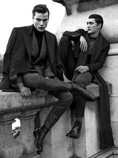 two men sitting on top of a stone wall next to each other wearing suits and ties