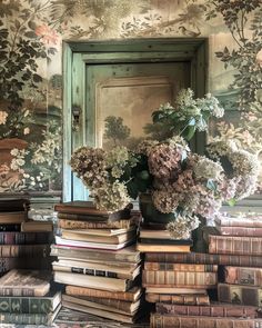 a bunch of books stacked on top of each other in front of a wall with flowers