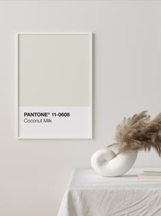 a white table topped with a vase filled with feathers next to a pantone poster