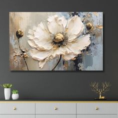 Textured painting of a large white flower with gold accents on a gray background. It hangs on a wall above a modern console with plants and decor.