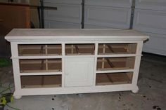 a white entertainment center with glass doors and shelves on the bottom, in a garage