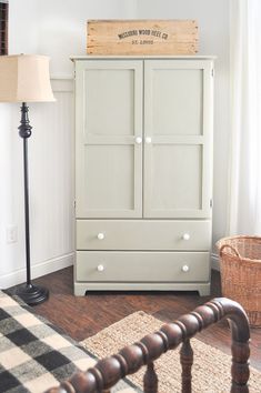 a white armoire sitting in a living room next to a lamp