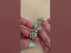 a person is holding a green and white beaded cross brooch in their left hand