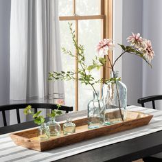 two vases with flowers are sitting on a wooden tray in front of a window