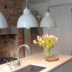 a kitchen with two lights hanging over the sink and flowers in a vase on the counter