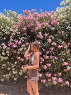 a woman standing in front of a bush with pink and white flowers on it's side