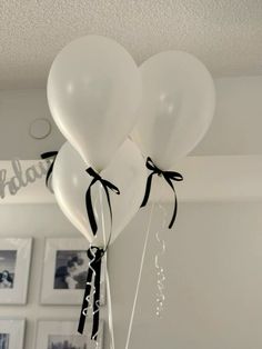 three white balloons with black ribbons tied to them hanging from the ceiling in a room