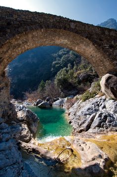 an old stone bridge over a small pool in the middle of a rocky mountain area