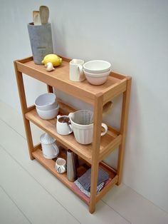 a wooden shelf with bowls, cups and utensils sitting on top of it