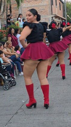 several women in short skirts and red socks are dancing on the street while people watch