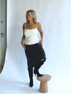 a woman standing on top of a stool in front of a white wall wearing a black skirt