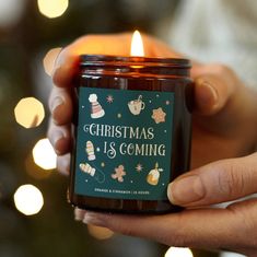 a person holding a candle in front of a christmas tree with lights on it and the words, christmas is coming