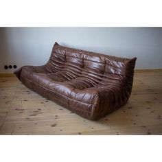 a brown leather couch sitting on top of a hard wood floor next to a wall