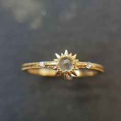 a yellow gold ring with an oval stone and two small diamonds on the band, sitting on a black surface