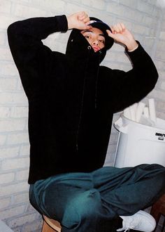 a young man sitting on top of a wooden stool in front of a brick wall