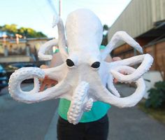 an octopus stuffed animal being held by a woman on the side of the road in front of a building