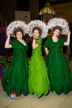 three women in green dresses are posing for the camera with white feathers on their heads