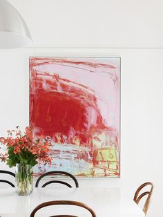 a dining room table with chairs and a large painting on the wall behind it that has red flowers in a vase