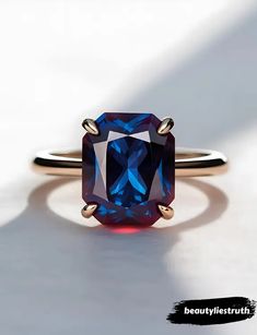 a ring with a blue and red stone on it's side, sitting on a white surface