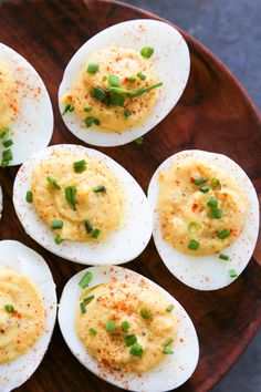 deviled eggs with chives and seasoning on a wooden plate, ready to be eaten