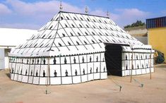 a large white tent with black and white designs on it's sides, in front of a yellow building