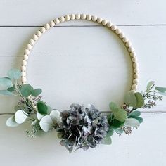 a wooden beaded wreath with flowers and greenery hanging from the front on a white wall