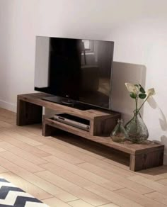 a flat screen tv sitting on top of a wooden stand next to a vase with flowers