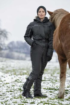 a woman standing next to a brown horse on top of a snow covered grass field