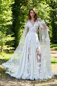 a woman wearing a white wedding gown with sheer sleeves and flowers on the side, standing in