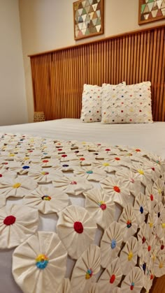 a bed with white bedspread covered in multicolored paper flowers on it