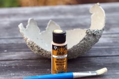 an egg shell next to a paintbrush on a wooden table