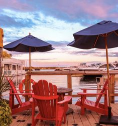 two red chairs sitting on top of a wooden deck next to an umbrella covered table