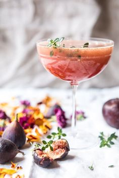 a table topped with a wine glass filled with liquid next to figs and flowers