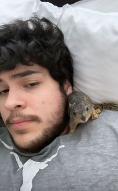 a man laying in bed with a squirrel on his shoulder