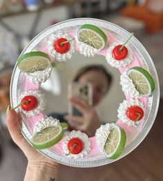 a person taking a selfie in front of a mirror holding a cake with limes and cherries on it