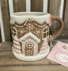 a ceramic mug with a gingerbread house on it and a card next to it