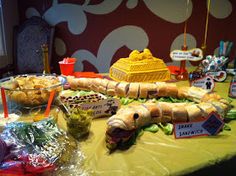 a table topped with lots of sandwiches and other foods on top of a yellow table cloth