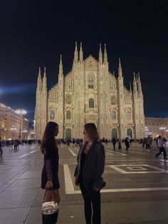 two women standing in front of a cathedral at night