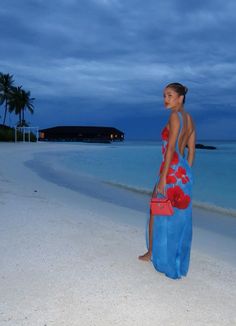 a woman in a blue dress standing on the beach at night with palm trees behind her