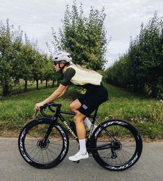 a man riding a bike down a street next to an apple tree filled orchard on a cloudy day