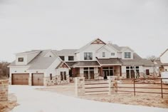 a large white house sitting on top of a snow covered field next to a wooden fence