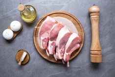 raw meat on a wooden plate next to an egg and butter shaker with two eggs in the background