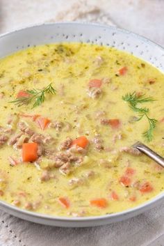 a bowl of soup with meat and carrots on a white cloth next to a spoon