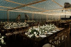 an indoor wedding setup with white flowers and greenery on the tables, along with string lights