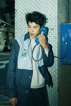 a young man talking on the phone while standing in front of a wall with tiles